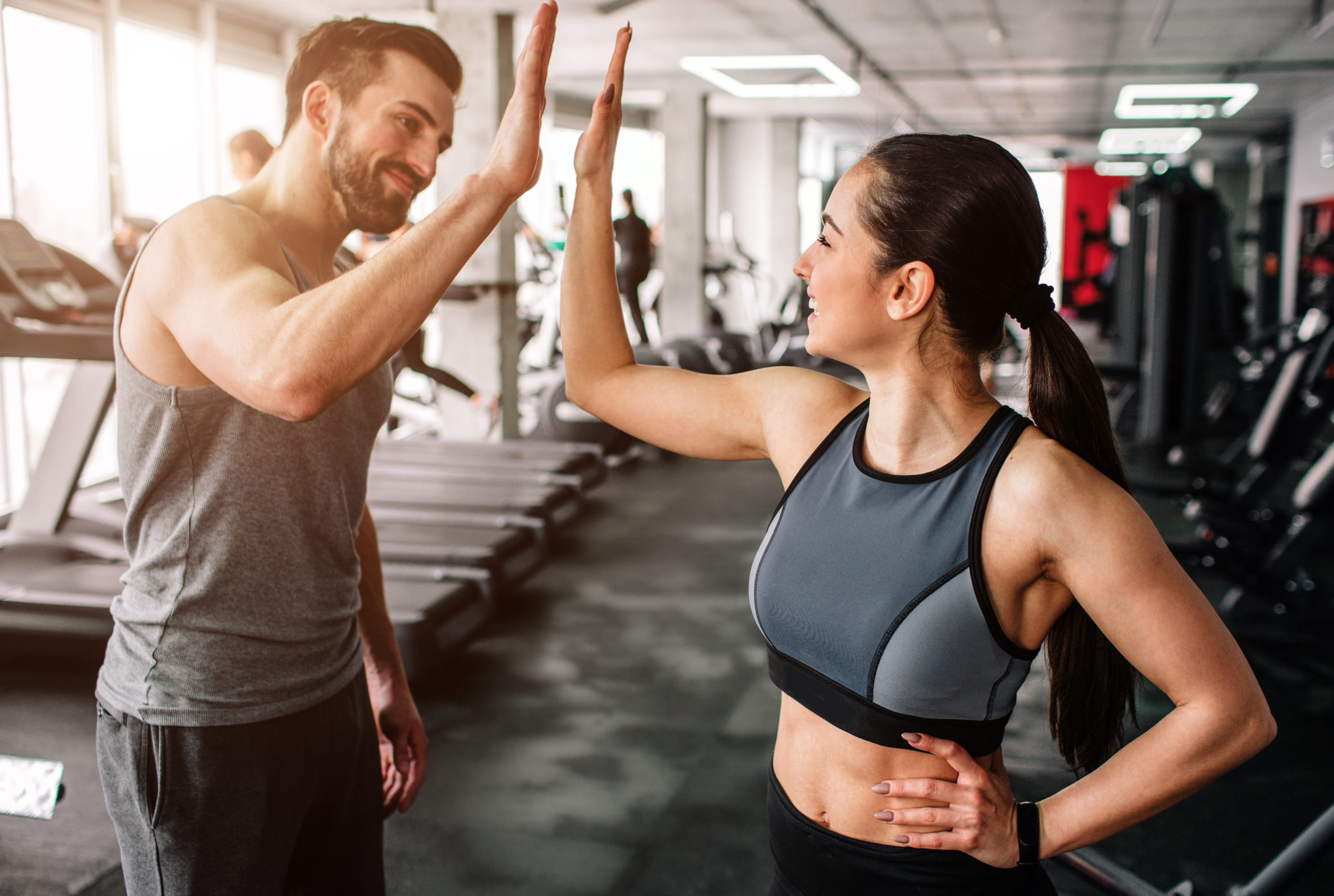 A beautiful girl and her well-built boyfriend are greeting each other with  a high-five. They are happy to see each othr in the gym. Young people are  ready to start their workout. -